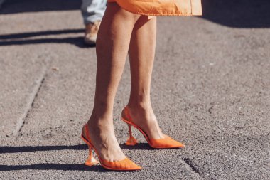 Milan, Italy - February 25, 2022: Woman in orange dress and high heeled shoes.
