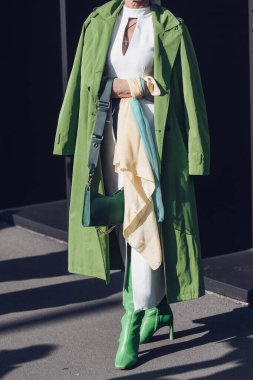 Milan, Italy - February 25, 2022: Female wearing a green coat, white dress, matching green bag and green high heels boots.