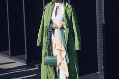 Milan, Italy - February 25, 2022: Female wearing a green coat, white dress, matching green bag and green high heels boots.