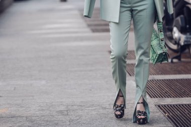 Female wearing light green pants, ornamental shoes and matching handbag.