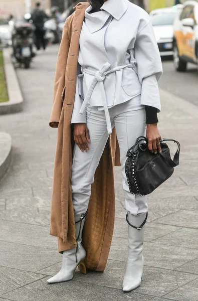 Milan, Italy - February 24, 2022: Woman model in white outfit with camel beige coat over shoulder holding handbag.