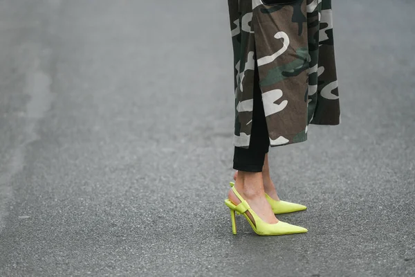 Milan, Italy - February 24, 2022: Woman in long dress with camouflage print pants and high heeled yellow shoes standing on pavement during fashion week
