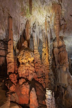 Postojna mağarasında yoğun kırmızı ve turuncu sütunlar. Beyaz noktalar su damlacıklarındaki ışığı yansıtır.