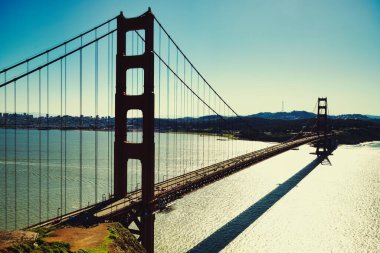 Etkileyici bir fotoğraf Golden Gate Köprüsü 'nün yan görüntüsünü sergiliyor ve arka planda yavaş yavaş kayboluyor. Görüntü çarpıcı bir şekilde köprüleri özetliyor.
