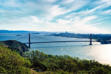 Dehşet verici panoramik bir fotoğraf ikonik Golden Gate Köprüsü 'nün tüm açıklığını gösteriyor. Parlak mavi bulutlarla kaplı gökyüzü altında mükemmel çerçevelenmiş. Görüntü sadece görüntüyü kapsamıyor.