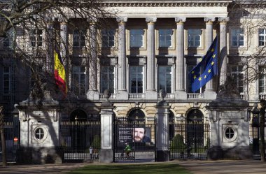 Bu resim, Belçika ve Avrupa Birliği bayraklarıyla süslenmiş görkemli bir binanın hem ulusal hem de uluslararası aralarındaki önemi ve bağlantısını simgeliyor.