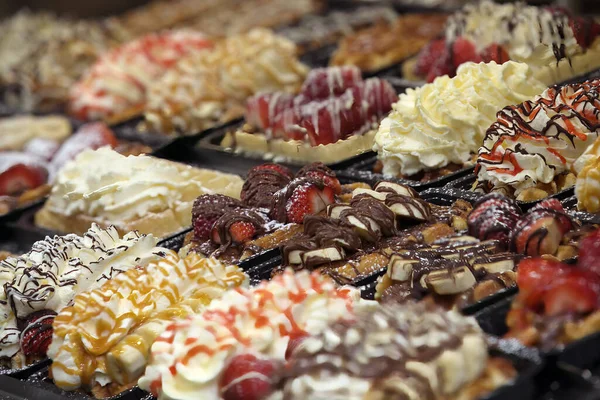 Bu cazip görüntü Belçika waffle çeşitlerinin her biri çeşitli meyveler, kremler ve çikolatalarla süslenmiş lezzetli bir çeşidini sergiliyor. Yakın çekim görüntüsü dokuları vurgular ve