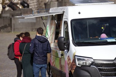 Canlı bir yemek kamyonunun önünde duran bir çift sokak yemeği seçmekle meşguldü. Servis penceresi açık olan yemek kamyonu yoldan geçenleri hızlı ve lezzetli bir yemek yemeye davet ediyor.