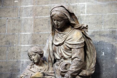 Bu anımsatıcı görüntü, Gent Katedrali 'nin kutsal sınırları içinde yer alan bir anne ve çocuğun taş heykelini yakalıyor. Anne, kabarık cübbeyle tasvir edilmiş, bir çocukla aşağı bakıyor