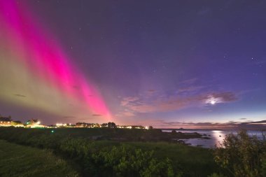 A stunning capture of the Aurora Borealis lighting up the sky over North Berwick coastline. The striking pink and green auroras contrast beautifully with the darkening sky and calm coastal waters clipart