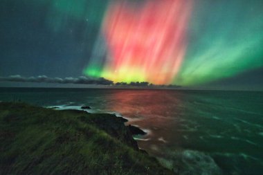 The ethereal Aurora Borealis lights up the night sky over the St. Abbs coastline in the UK. Shades of green and pink illuminate the scene, blending seamlessly with the dark, starry sky and reflecting clipart