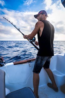 Genç adam bir beyzbol kap onboard geminin arka planı mavi deniz balık tutma sırasında.