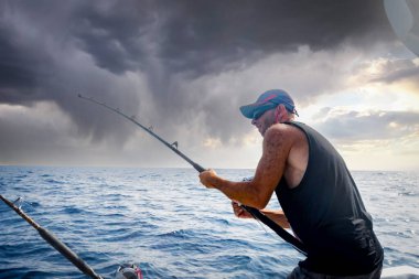 Genç adam bir beyzbol kap onboard geminin arka planı mavi deniz balık tutma sırasında.