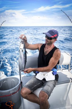 Genç adam bir beyzbol kap onboard geminin arka planı mavi deniz balık tutma sırasında.