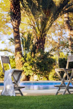 İki yüksek bar taburesi, dikkatsizce sol havluyla, yeşil çimlerin üzerindeki havuzun kenarında, batan güneşin aydınlattığı palmiye ağaçlarının altında..