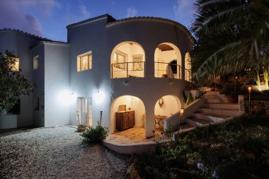 Günbatımında beyaz villa, akşam geç saatlerde, sıcak pencere aydınlatması.