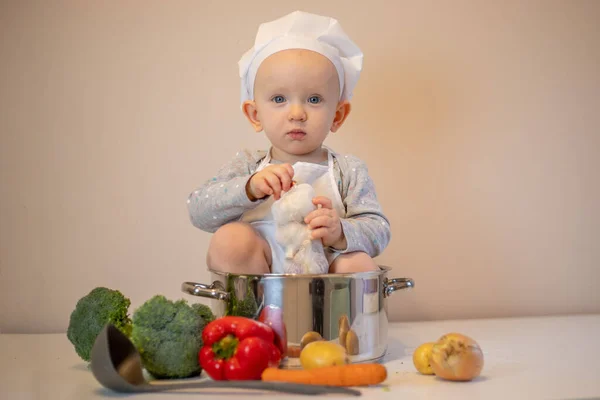Little female chef preparing vegetable soup in kitchen.