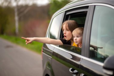 Mutlu erkek ve kız kardeş araba camından dışarı bakar, parmağını yana doğru tutar ve şaşırır.