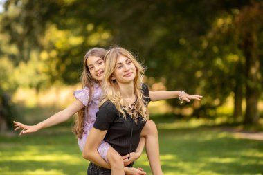 Anne, kızını sırtında taşıyor ve gülümsüyor..