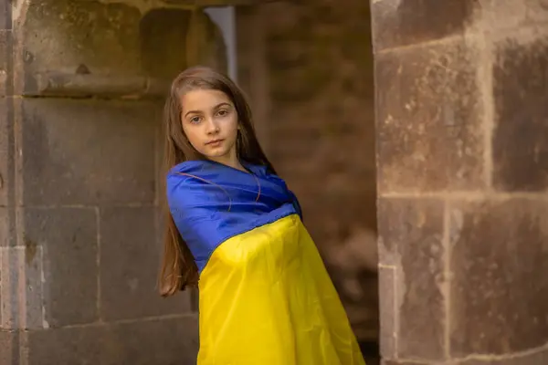 Girl in Ukrainian flag looking afar standing by an ancient wall.
