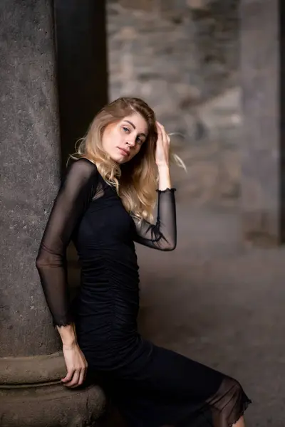 Girl in black dress leaning on a column.