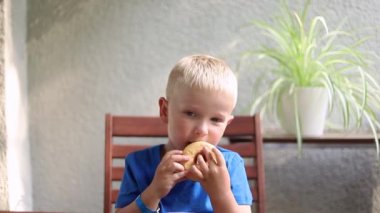 Küçük çocuk evde masada otururken donut yiyor..