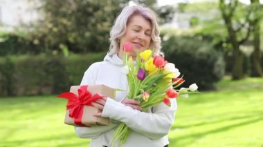 Dışarıda elinde lale ve kırmızı kurdeleli bir hediye tutan kadın.