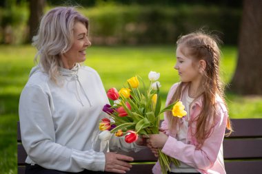 Kızım anne laleleri veriyor, ikisi de dışarıda gülümsüyor..
