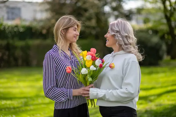 Córka Daje Matce Tulipany Zarówno Uśmiechnięte Zewnątrz — Zdjęcie stockowe