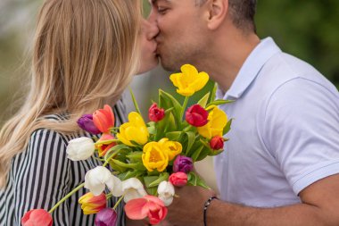 Bahar parkında öpüşen, bir buket renkli lale tutan sevgili çift..