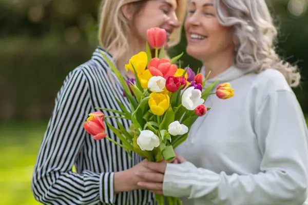 stock image Daughter hugs mother, focus on tulip bouquet.