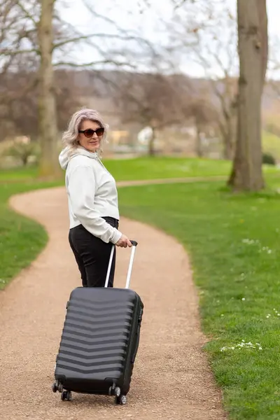 Woman with a suitcase smiles looking over shoulder on a park alley