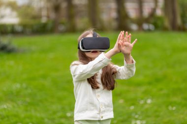 Sanal gerçeklikteki kız parkta el kaldırıyor..