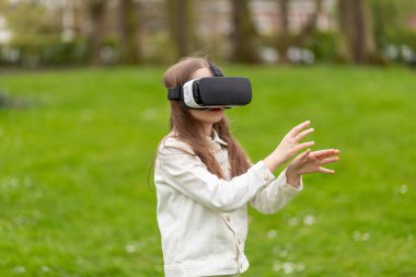 Parkta kollarını açmış sanal gerçeklik kulaklığı takan bir kız..