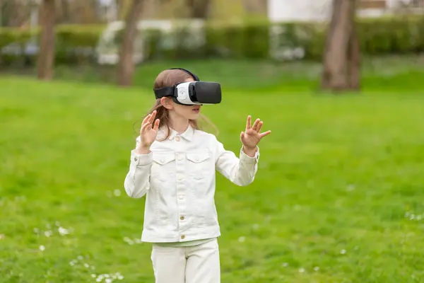 stock image Girl in virtual reality headset with arms outstretched in a park.