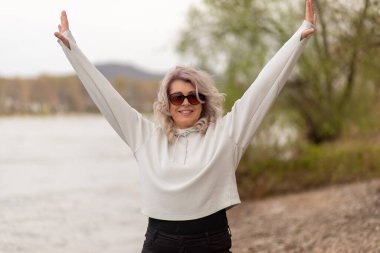 Mutlu olgun kadın nehir kenarında el kaldırıyor..
