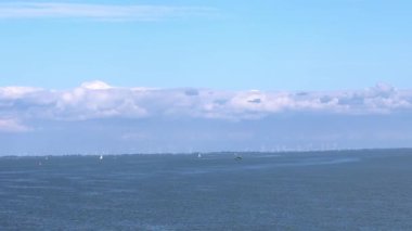 Yelkenliler sakin sularda yol alırken, kabarık bulutlar yaz günlerinde sakin bir sahil bölgesinde mavi gökyüzünde sürüklenir..
