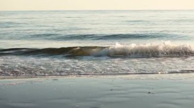 Gün batımının altın ışığı altında sakin bir atmosfer yaratarak plaja vuran rahatlatıcı dalgaları izleyin. Tecrübe doğası sakinleştirici güzellik.