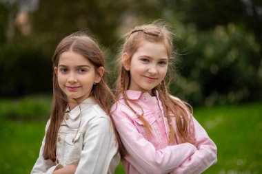 Pastel renkli kıyafetler giymiş iki genç kız arka planda sırt sırta dururlar.