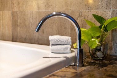 Sıcak bir banyoda, modern bir musluk yumuşak havlular ve küçük yeşil bir bitkinin yanında oturur. Huzurlu ve davetkar bir ortam yaratır..