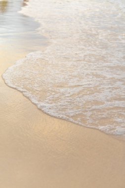Güneş sakin sahil şeridinde batıyor, yumuşak dalgalar kıyıya vururken, kumlara sıcak bir parıltı yayıyor, rahatlama ve yansıma için mükemmel huzurlu bir atmosfer yaratıyor..