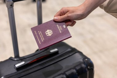 Gezgin, havaalanında siyah bir valizin yanında dururken bir pasaport tutuyor. Ayrılışından hemen önce yapılacak olan uluslararası maceraların heyecanını yakalıyor..