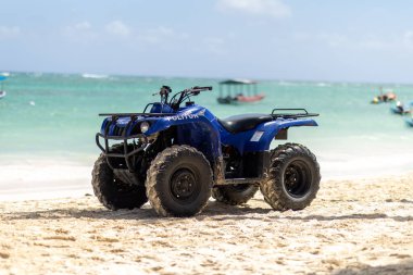 Punta Cana, Dominik Cumhuriyeti - Mart, 24, 2025: Okyanus manzaralı kumlu bir plaja mavi bir arazi aracı park edilmiştir. Güneşli bir günde açık mavi gökyüzünün altında kayıklar görülebilir..