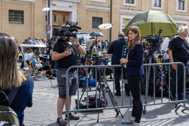 Vatikan - 23 Nisan 2025: Kadın muhabir mikrofon ve kameralarla canlı çekim için hazırlanıyor.