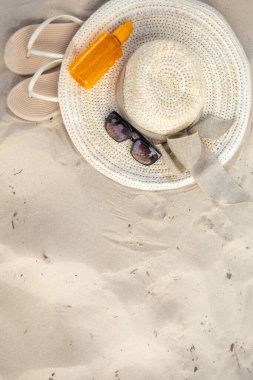 Güneş şapkası, parmak arası terlikler ve güneş gözlükleri açık havada bir güne hazırlanmak için yumuşak kumda dinleniyor. Güneş kremi, güneşlenmek isteyenler için ideal bir eğlence kaynağı..