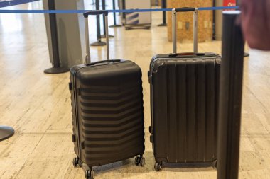Siyah, sert kabuklu bavullar havaalanında yan yana durur. Bavullar yolculuk için hazırken, yolcular da yoğun bir etkinliğin ortasında kuyruğa girdiler..