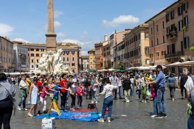 Rom, Italien - Nisan 23, 2025: Çocukların dev sabun köpüklerini kovaladığı tarihi bir plazada, yetişkinler seyrederken, açık mavi gökyüzü altında gülücükler ve kahkahalar paylaşırken, coşkulu bir kalabalık toplanır..