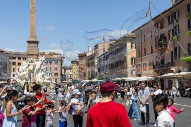 Rom, Italien - 23 Nisan 2025: Çocuklar ve aileler Roma Piazza Navona 'da toplanıyor, burada dev kabarcıklar havada yüzüyor. Kahkahalar güneşli kareyi doldurur eller uzanıp parıldayan yaradılışları ortaya çıkarırken.