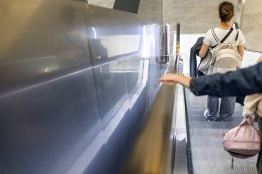 İyi ışıklandırılmış, modern bir binada yürüyen merdivende duran bir insan. Gösterişli tasarım, cilalı yüzeyler ve çağdaş bir atmosfer içeriyor. Mimari zarafet sergiliyor..