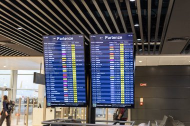 Fiumicino, Rom, Italien - 24 Nisan, 2025: Dijital ekranlar bir havaalanındaki varış, zaman ve uçuş durumları da dahil olmak üzere uçuş bilgilerini göstermektedir. Gezginler hareketli terminaldeki uçuşlarını kontrol ederler..